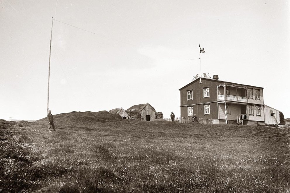 „Málmeyjarhúsið 25. júní 1931. Hér er húsið 6 ára gamalt og í sínu besta standi. Hluti gamla bæjarins stendur enn ofan við og fjósbyggingin komin norðan undir. Búið er að draga fána að húni, líklega í tilefni myndatökunnar eða komu Arthurs Gook sem hefur gætt þess að útvarpsstöngin nyti sín á myndinni, enda upphaflega reist 1928 vegna útvarpsstöðvar hans. Þessi stöng virðist ætla að standa í heila öld og er enn árið 2020, það eina sem upp úr gnæfir á bæjarstæðinu. Einn fóstursonurinn er við stöngina en annar við húsgaflinn og líklega er það Gísli Konráðsson meðeigandi í Málmey sem ber við loft á myndinni. Hrúgaldið sunnan við húsið og grindverkið mun vera bænhústóftin og mótar vel fyrir bænhúsgarðinum í hálfhring utan um hana,“ segir Hjalti Pálsson, Byggðasöguritari, í myndatexta. MYND ÚR X. BINDI BYGGÐASGÖU SKAGFIRÐINGA