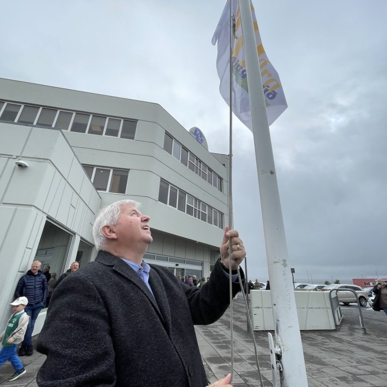 Pétur Pétursson flaggar í morgun líkt og hann gerði þegar búðin var fyrst opnuð árið 1983. Hann var yfirsmiður byggingarinnar. Mynd: SMH